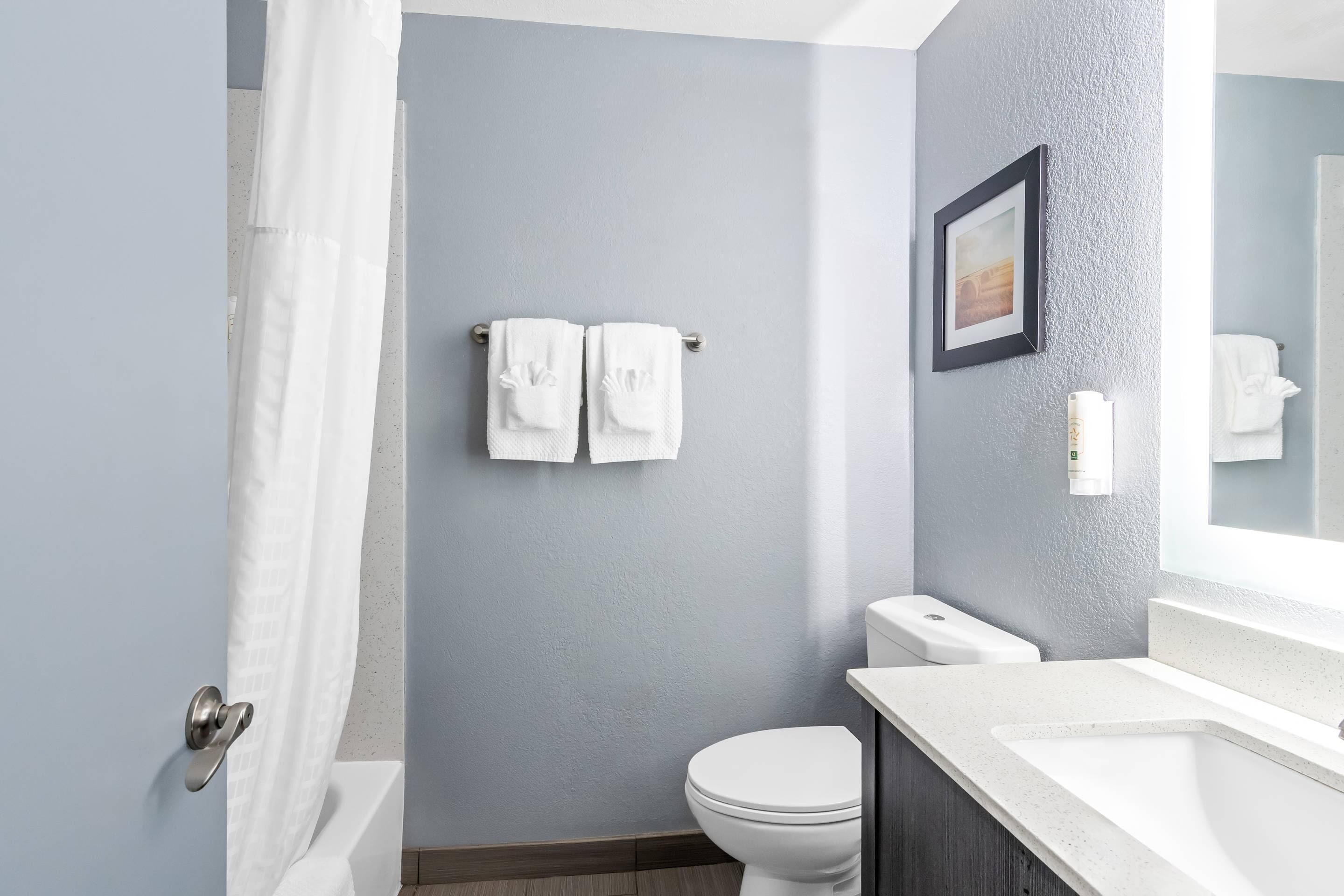 A bathroom with a toilet, a sink, a shower curtain, and towels on a rack.