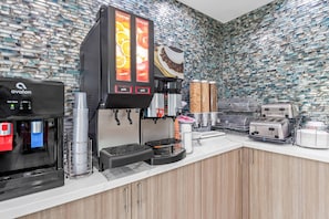 Une machine à café autonettoyante, un distributeur de boissons au style rétro et un grille-pain posés sur un comptoir, le tout agrémenté d’un pare-éclaboussures à motifs.