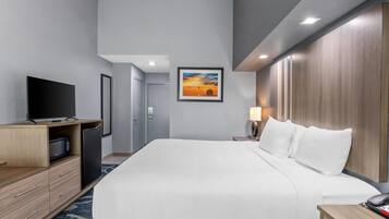A hotel room with a large bed, a TV, a desk with a lamp, and a painting on the wall.
