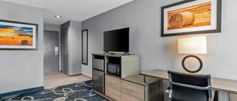 A hotel room with a desk, a television, a cabinet, a patterned rug, and framed pictures on the walls.