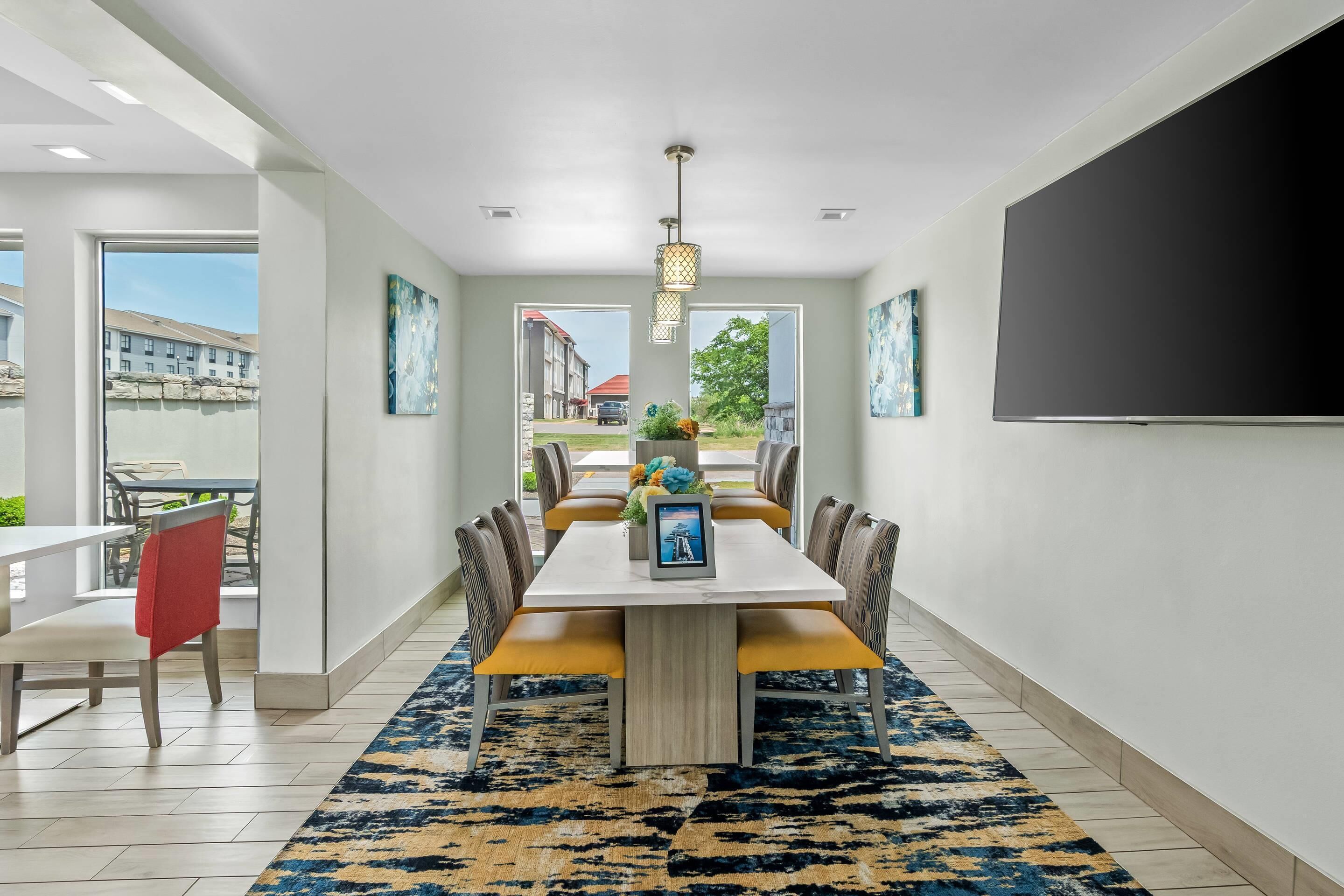 A dining area with a table, chairs, a rug, and a TV on the wall.