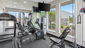 Ein Fitnessraum mit Cardiogeräten, Gewichtsbänken und einem Fernsehbildschirm.