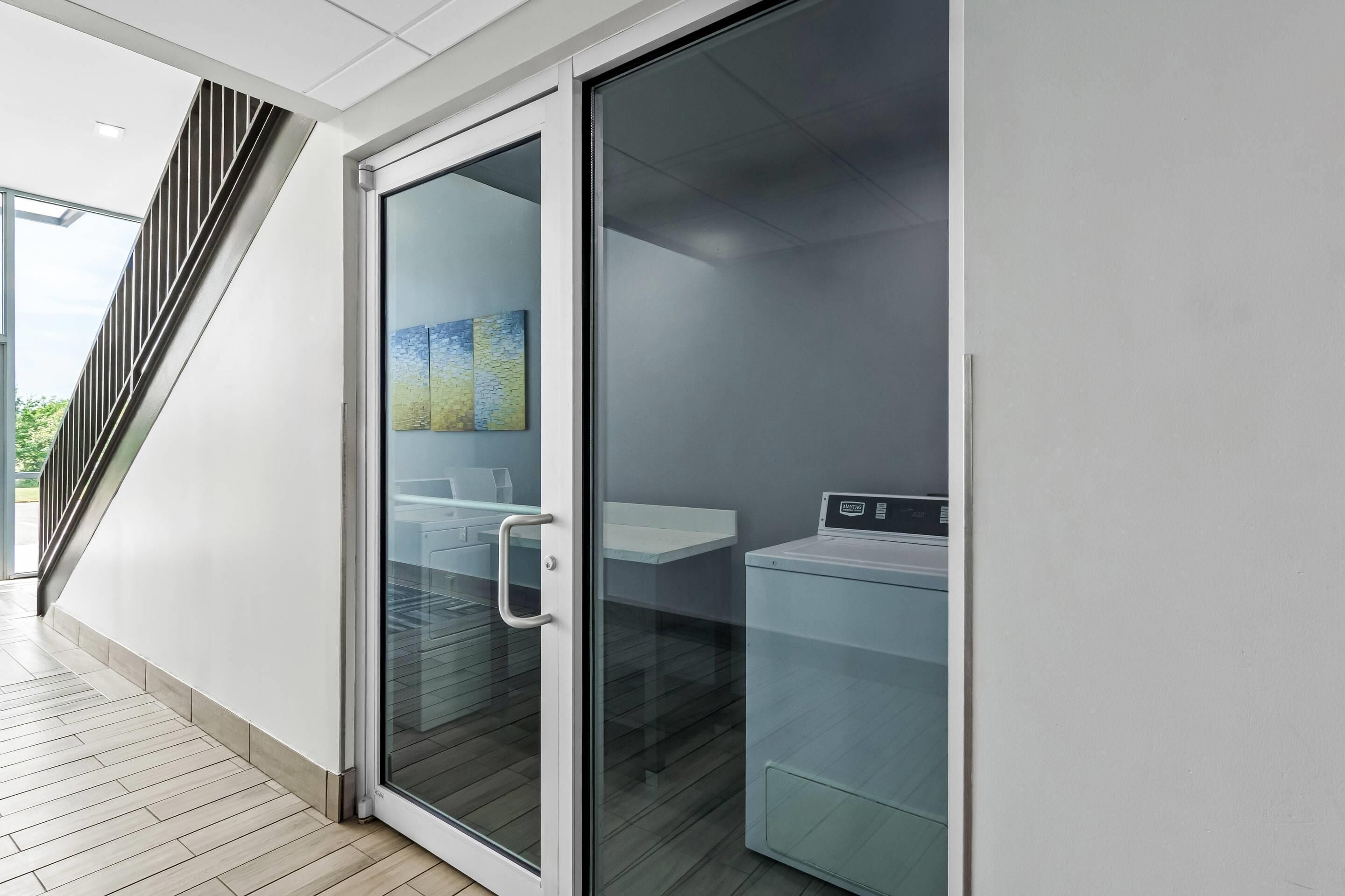A modern interior with a glass door leading to a laundry area, a staircase, and a view of greenery outside.