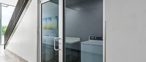 A modern interior with a glass door leading to a laundry area, a staircase, and a view of greenery outside.