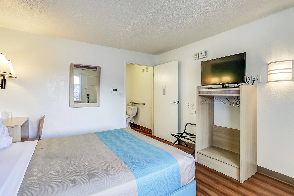 A hotel room with a bed, a TV, a wardrobe, and a bathroom visible through an open door.