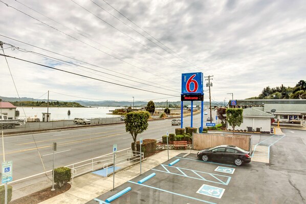 A motel sign, parking lot, and a view of the road and water. - Motel 6 Coos Bay, OR (Coos Bay)