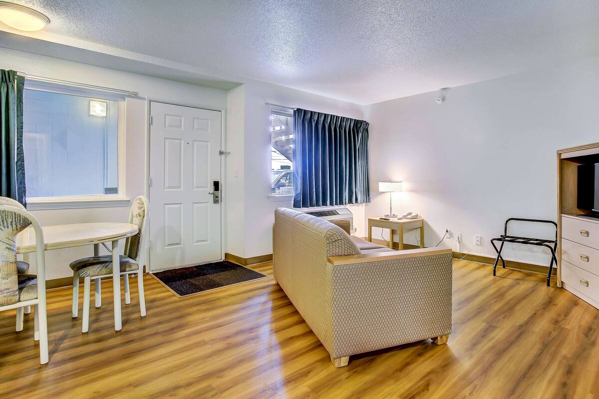A room with a wooden floor, a sofa, a dining table with chairs, a TV, and a window with curtains.