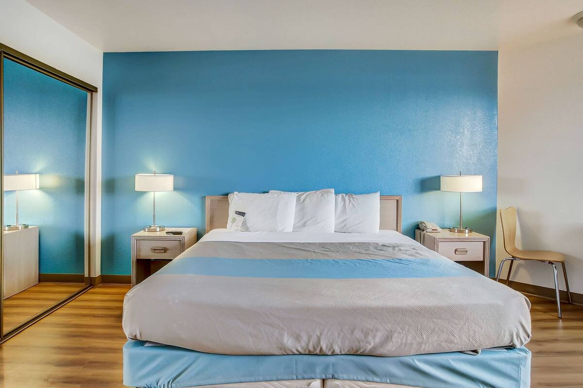 A hotel room with a large bed, two bedside tables with lamps, a chair, and a mirror.
