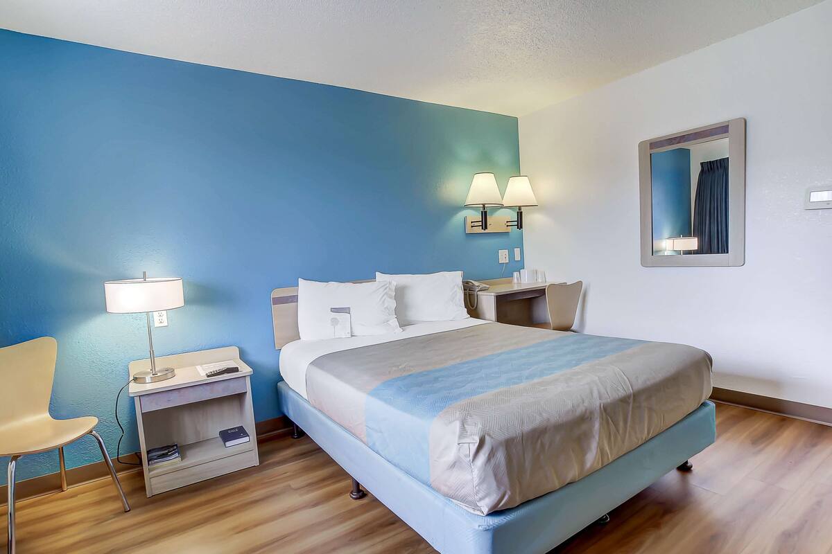 A hotel room with a bed, bedside tables, a chair, and a desk with a lamp.