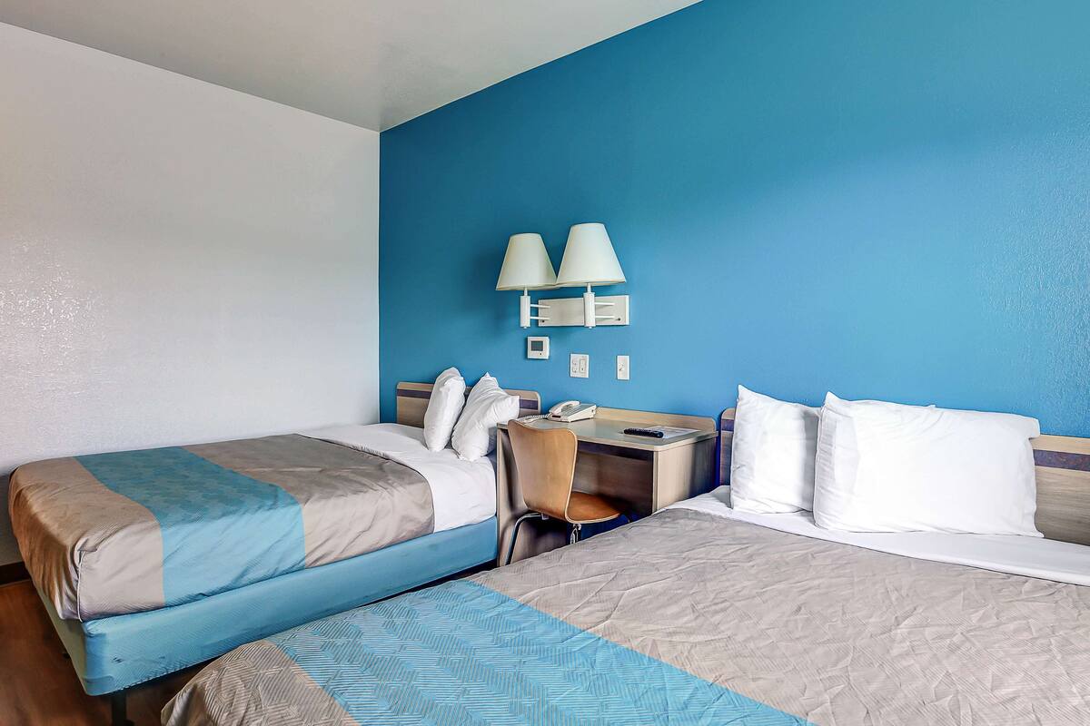 A hotel room with two beds, a desk, a chair, a lamp, and a phone.