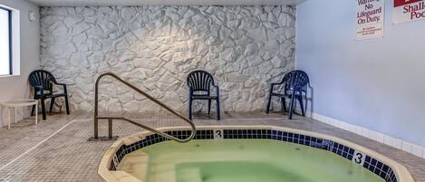 A pool area with a stone wall, three chairs, and a lifeguard sign.