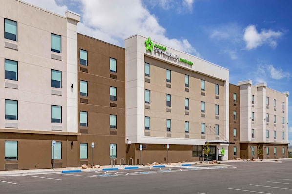 A multi-story hotel with a modern design, featuring a prominent green logo and the name 'STAY AMERICA Premier Suites' on the facade.