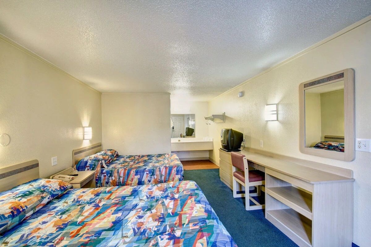 A hotel room with two beds, a desk, a chair, a television, and a mirror.