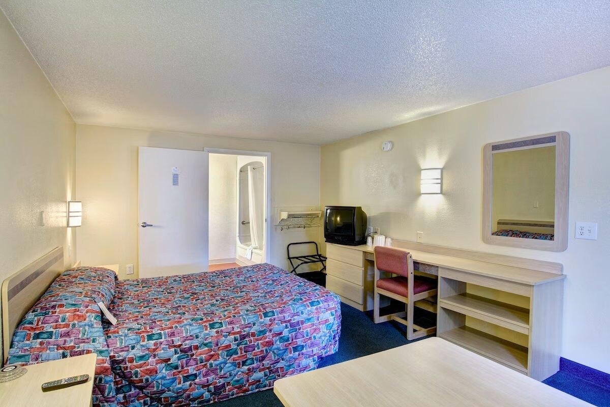 A hotel room with two beds, a desk, a chair, a television, and a mirror.
