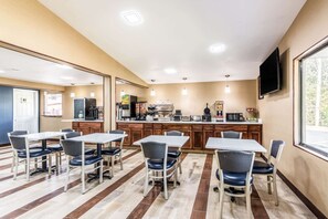 A dining area with tables and chairs, a kitchen in the background, and a TV mounted on the wall. - Econo Lodge Gastonia North (Gastonia)
