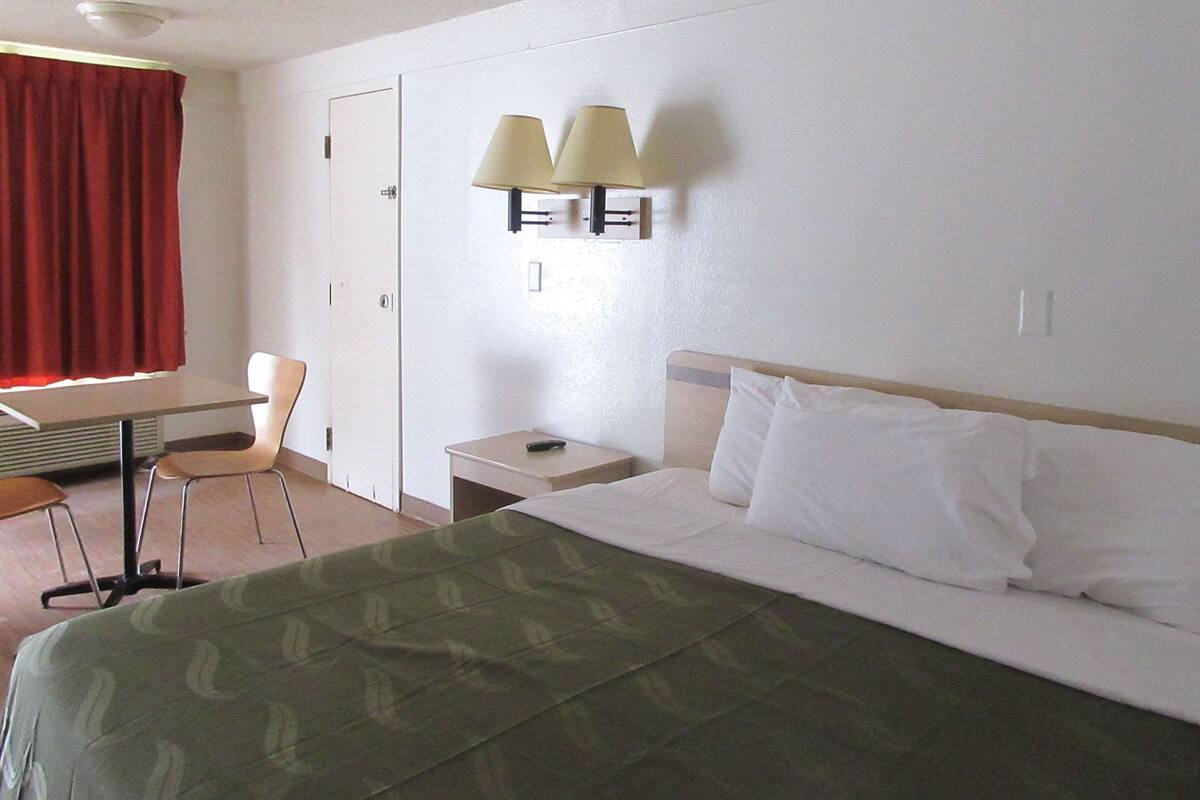 A hotel room with a bed, a desk with a chair, a nightstand, and two wall-mounted lamps.