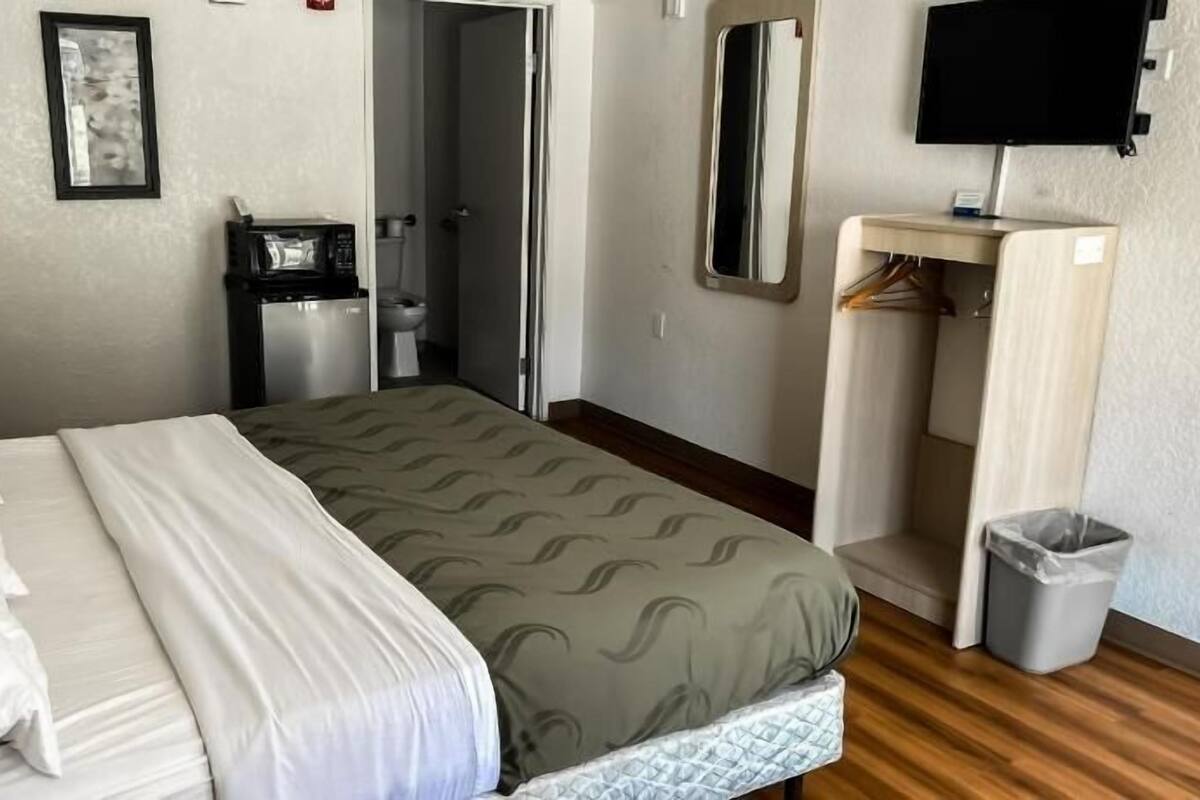 A hotel room with a bed, a desk, a mirror, a television, and a bathroom.