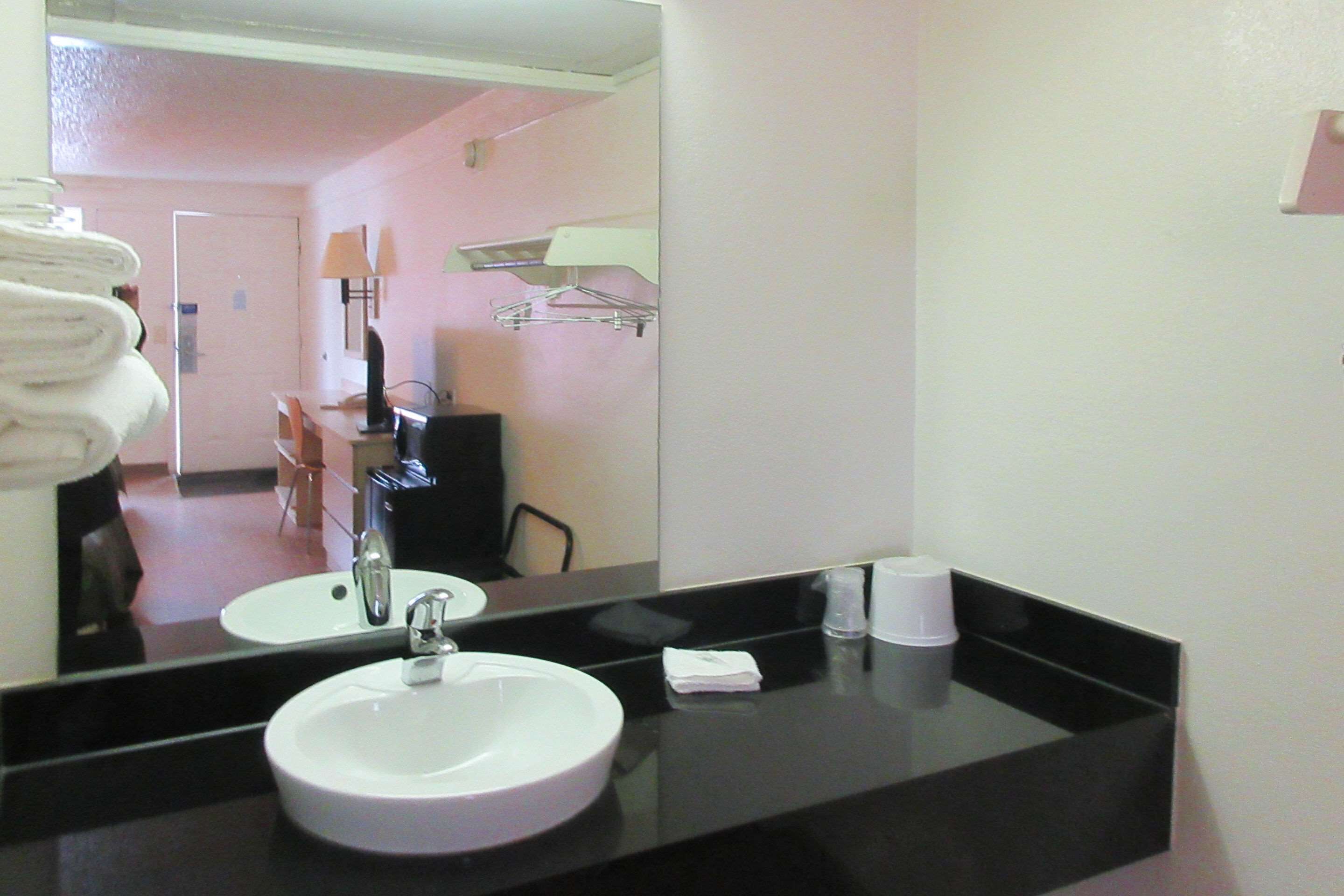 A hotel bathroom with a round sink, a mirror, a towel rack with folded towels, a small towel, and a cup.