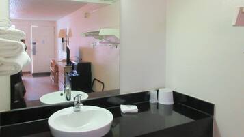 A hotel bathroom with a round sink, a mirror, a towel rack with folded towels, a small towel, and a cup.