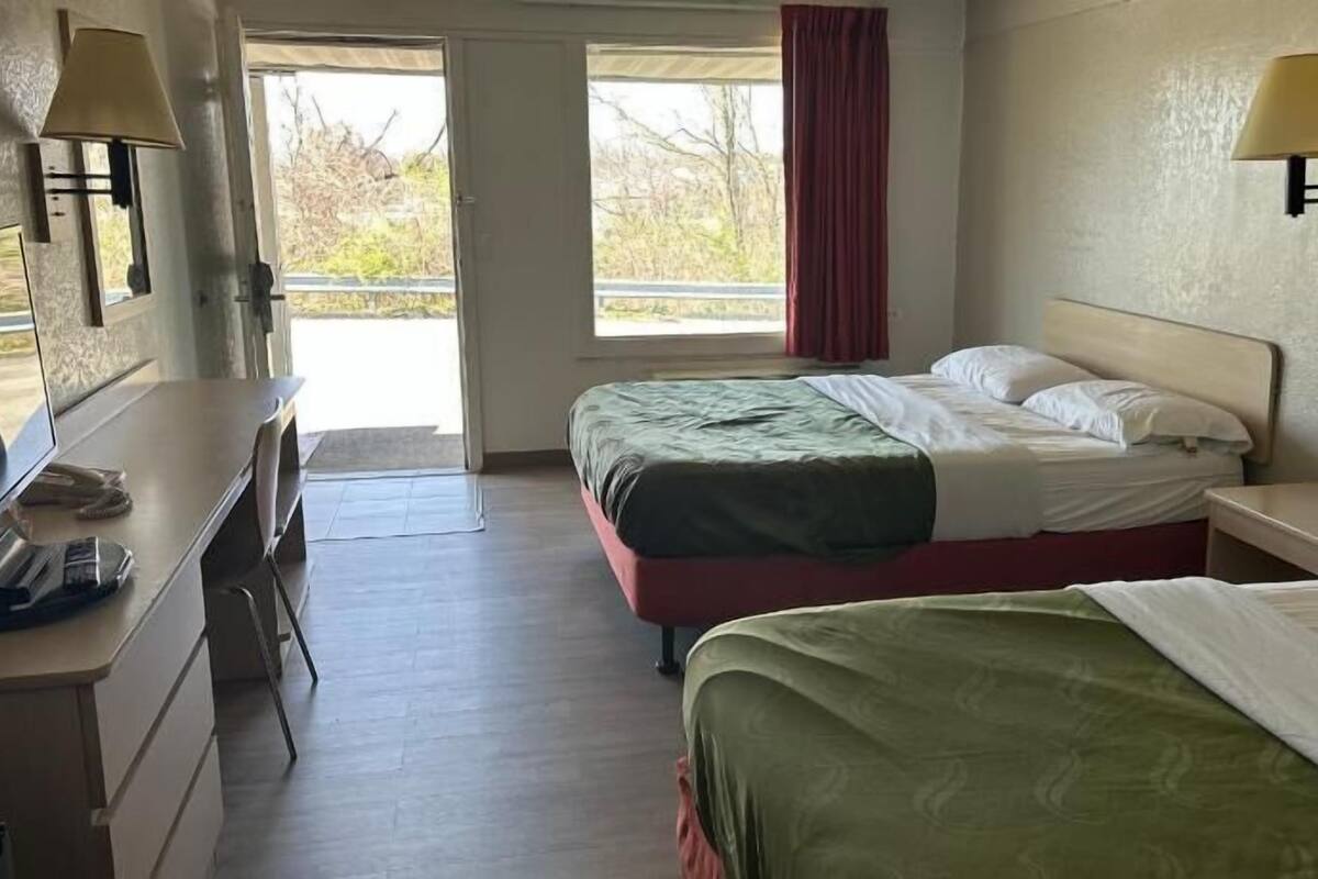 A hotel room with two beds, a desk with a telephone, and two wall-mounted lamps.