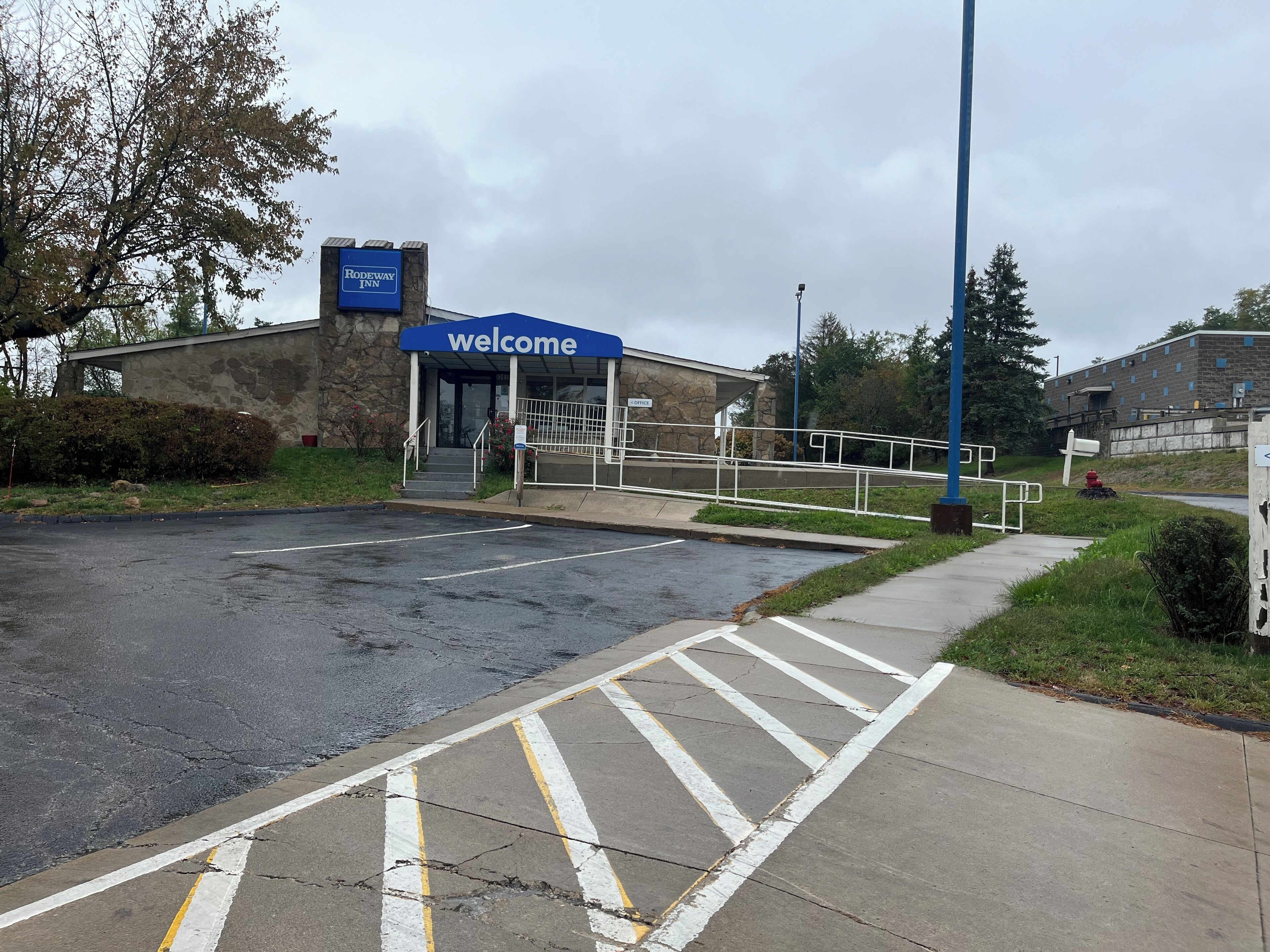 A parking lot with a 'Welcome' sign, a building entrance, and a pedestrian pathway.
