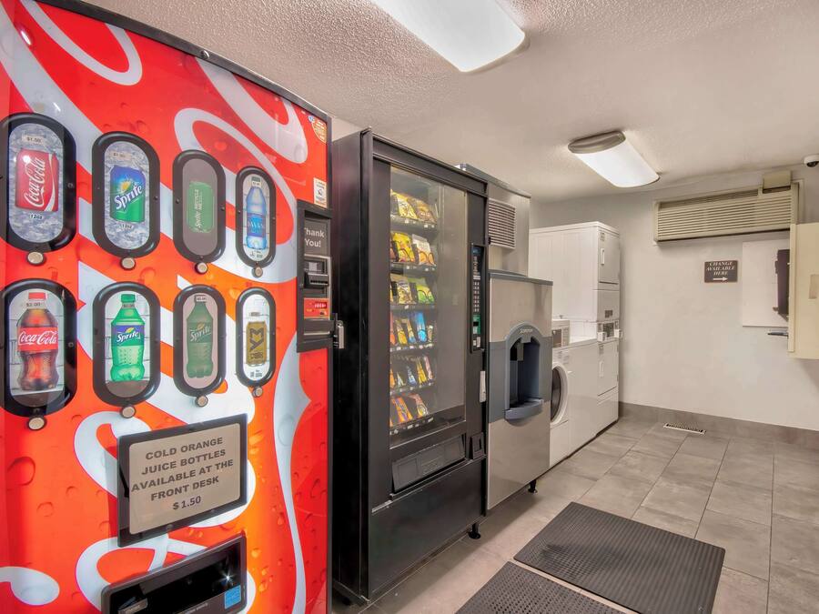 A vending machine with Coca-Cola and Sprite options, a self-service beverage dispenser, and a sign for cold orange juice at the front desk.