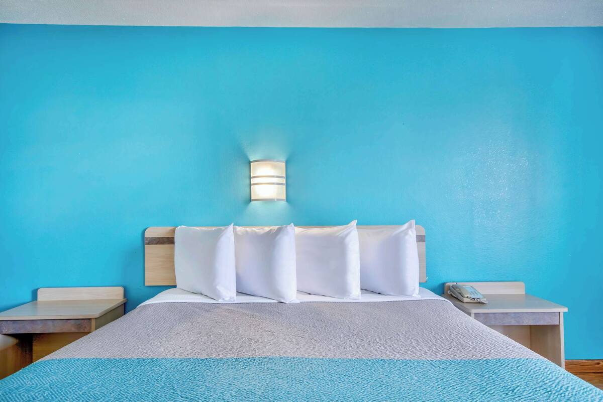 A hotel room with a bed, a nightstand, a wall-mounted light, and a telephone.