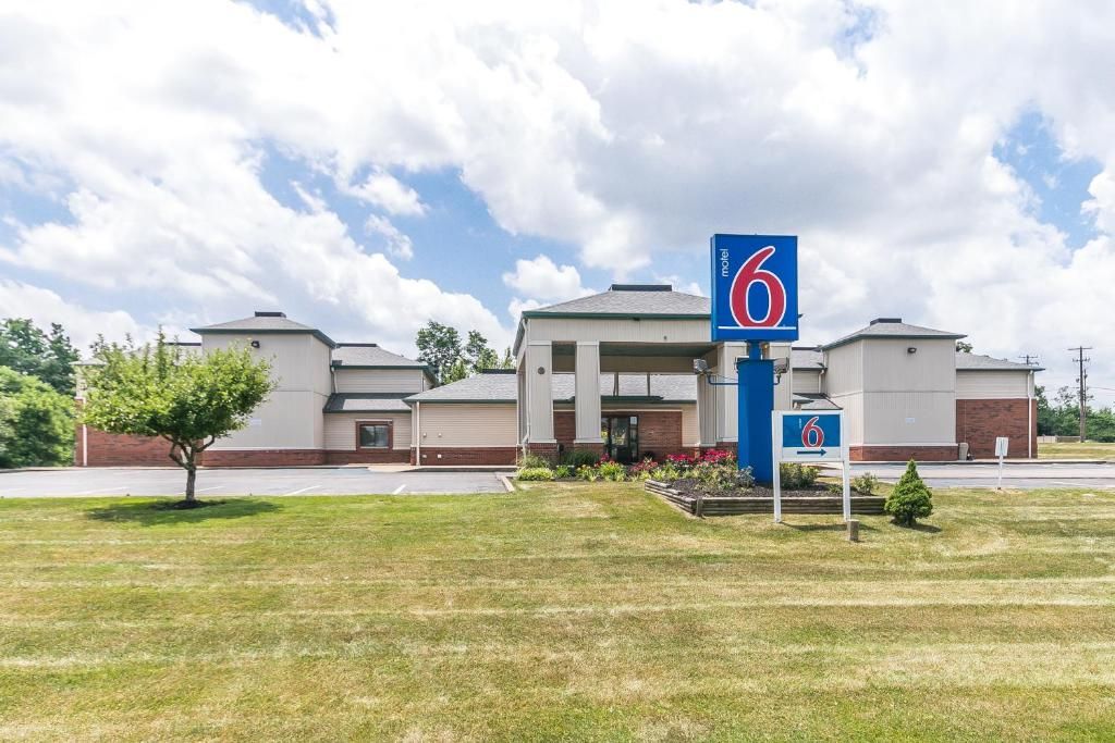 A motel with a prominent '6' sign, a parking lot, and a grassy area in front.