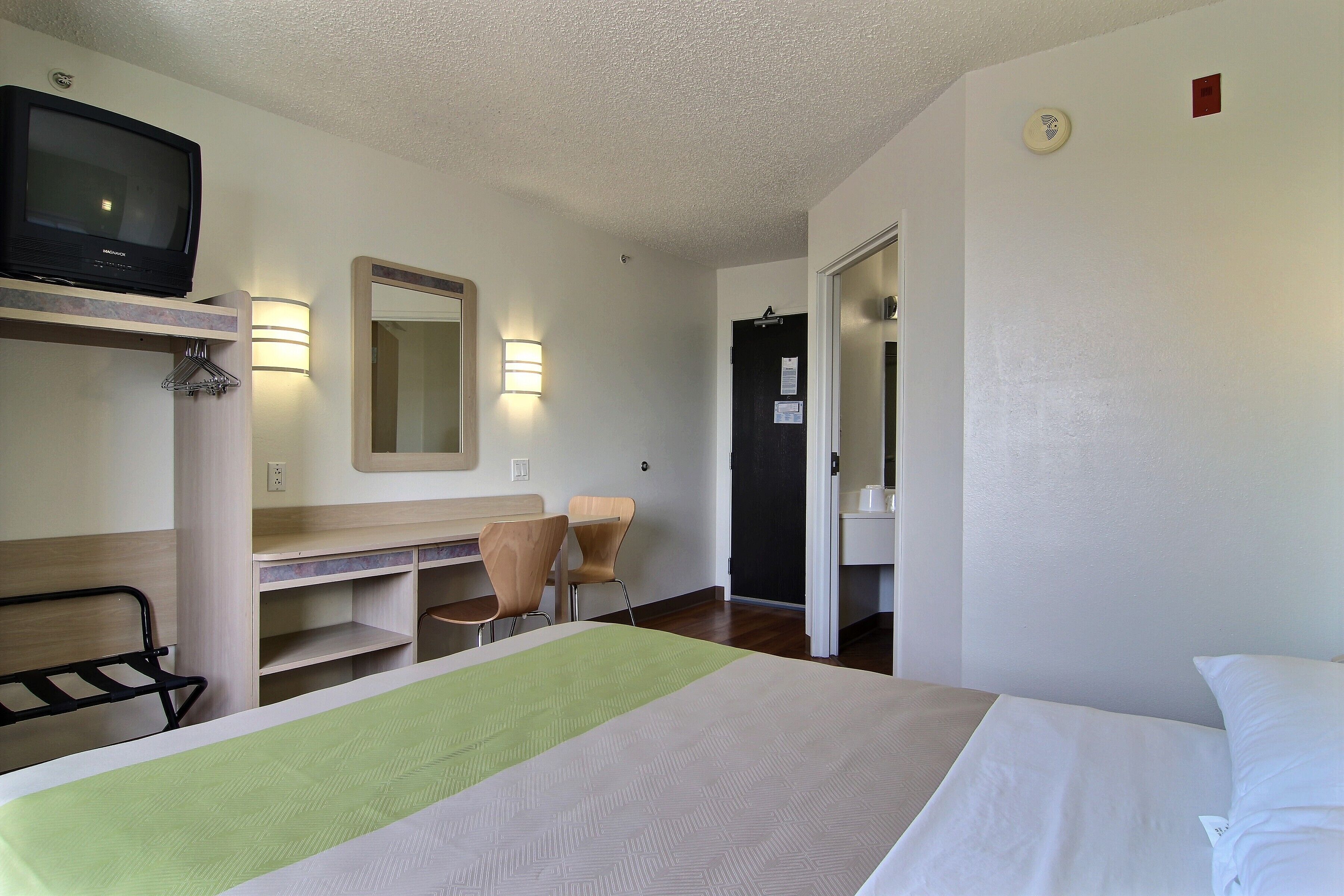 Een hotelkamer met een bed, een bureau, een stoel, een televisietoestel en een spiegel.