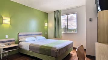 Une chambre d’hôtel comprenant un lit, une table de chevet avec un téléphone, une chaise, une fenêtre avec vue et un climatiseur fixé au mur.