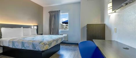 A hotel room with a bed, a desk, a chair, a window with curtains, and a view of the outside.