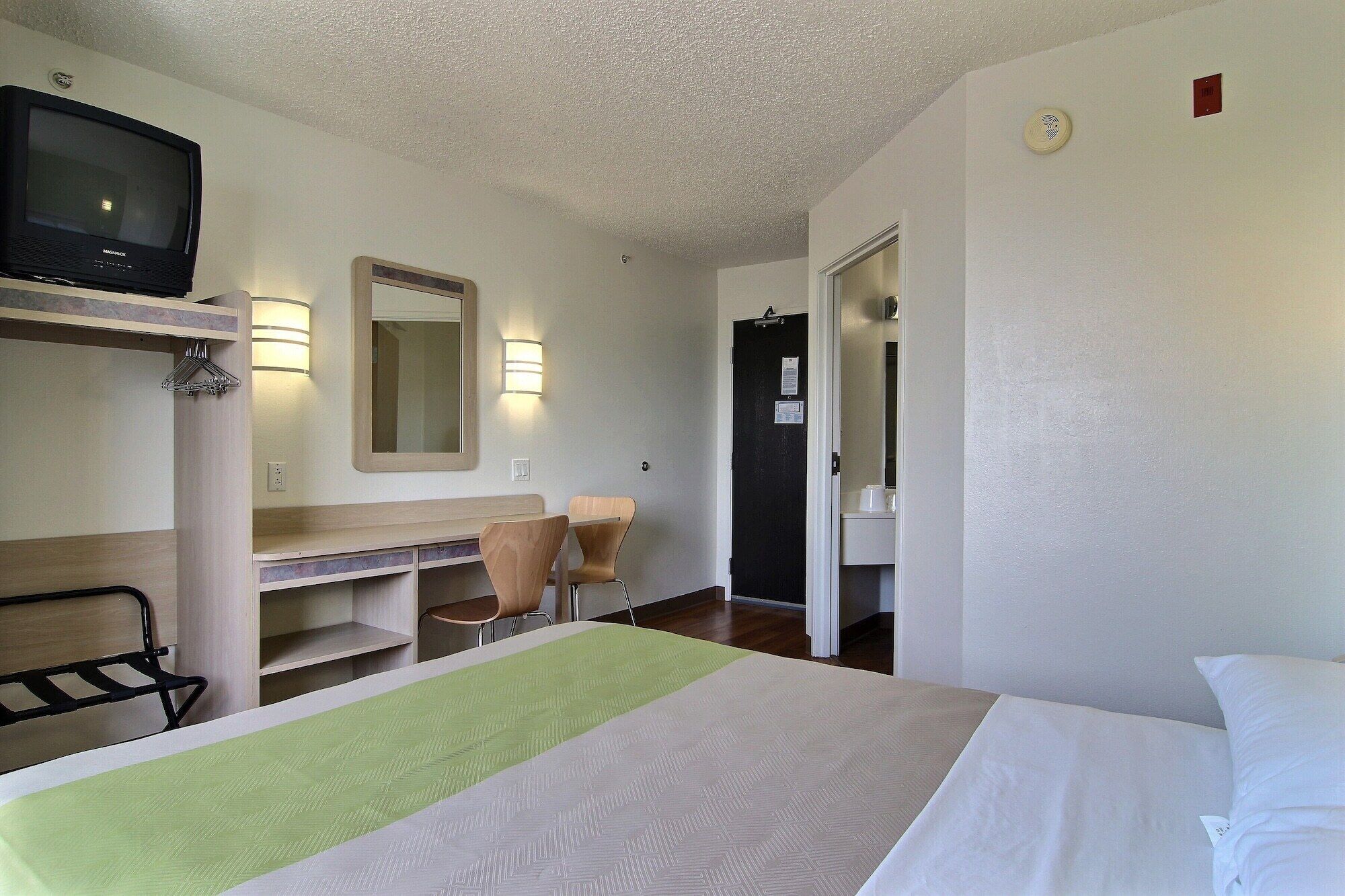 A hotel room with a bed, a desk, a chair, a television, and a mirror.