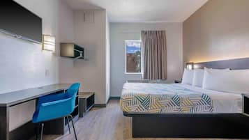 A hotel room with a bed, a desk, a chair, a TV, and a window with curtains.