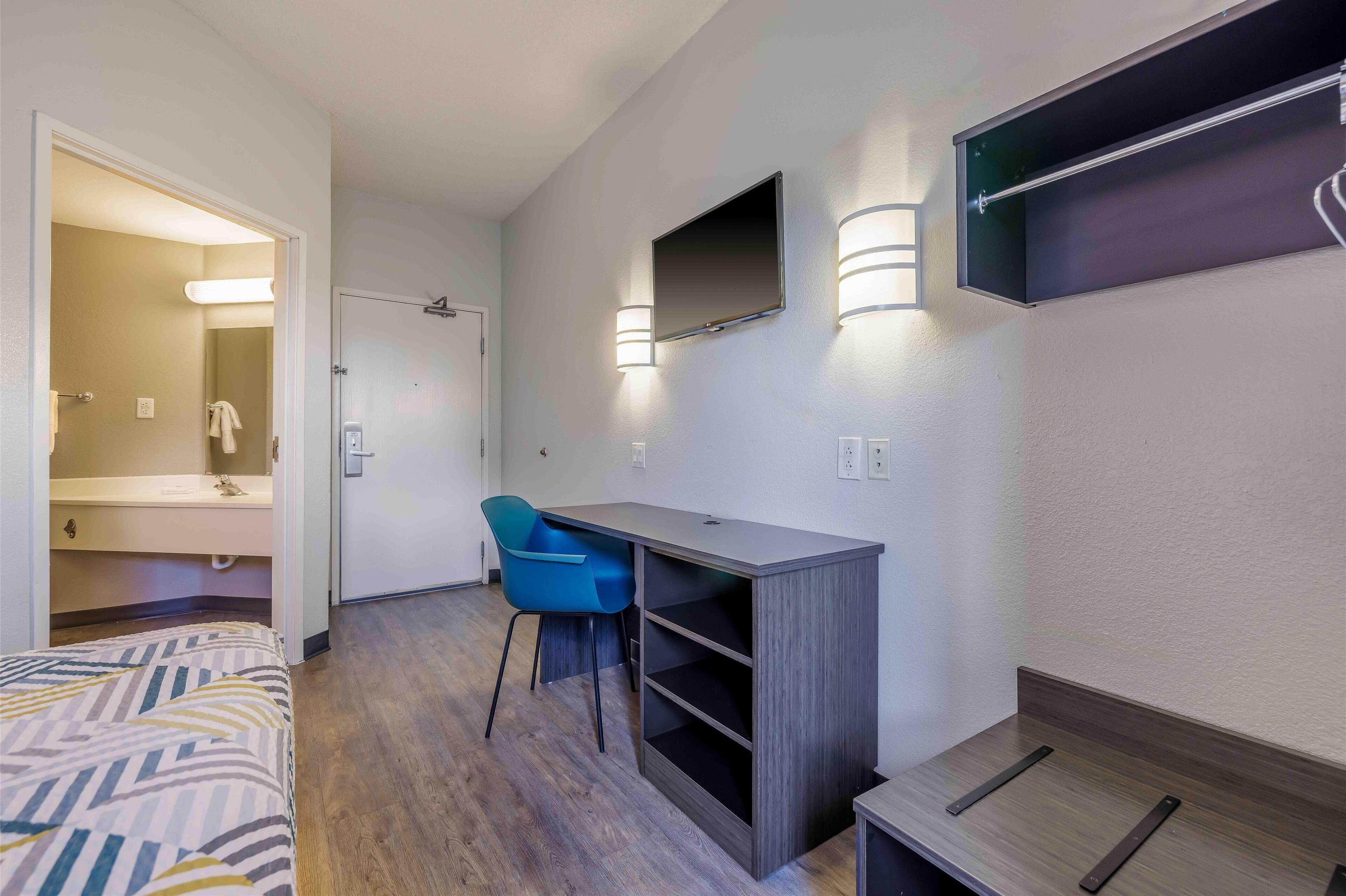 Camera d'albergo con un letto, una scrivania, una sedia, una TV a parete e un angolo doccia.
