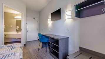 Camera d'albergo con un letto, una scrivania, una sedia, una TV a parete e un angolo doccia.