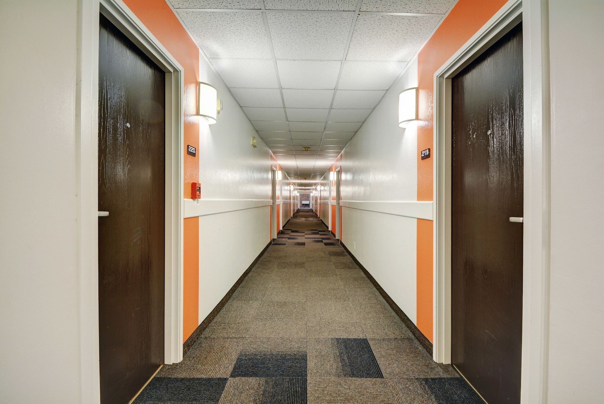 A long, narrow hallway with carpeted floors, white walls, and orange accents.