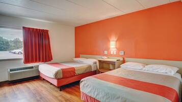 Habitación de hotel con dos camas, un escritorio, una silla, una ventana con cortinas y una lámpara de pared.