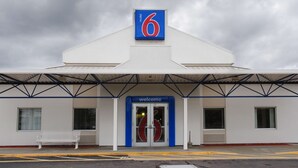 Un motel con un letrero que dice '6', una entrada con la palabra 'Welcome' y una banca afuera.