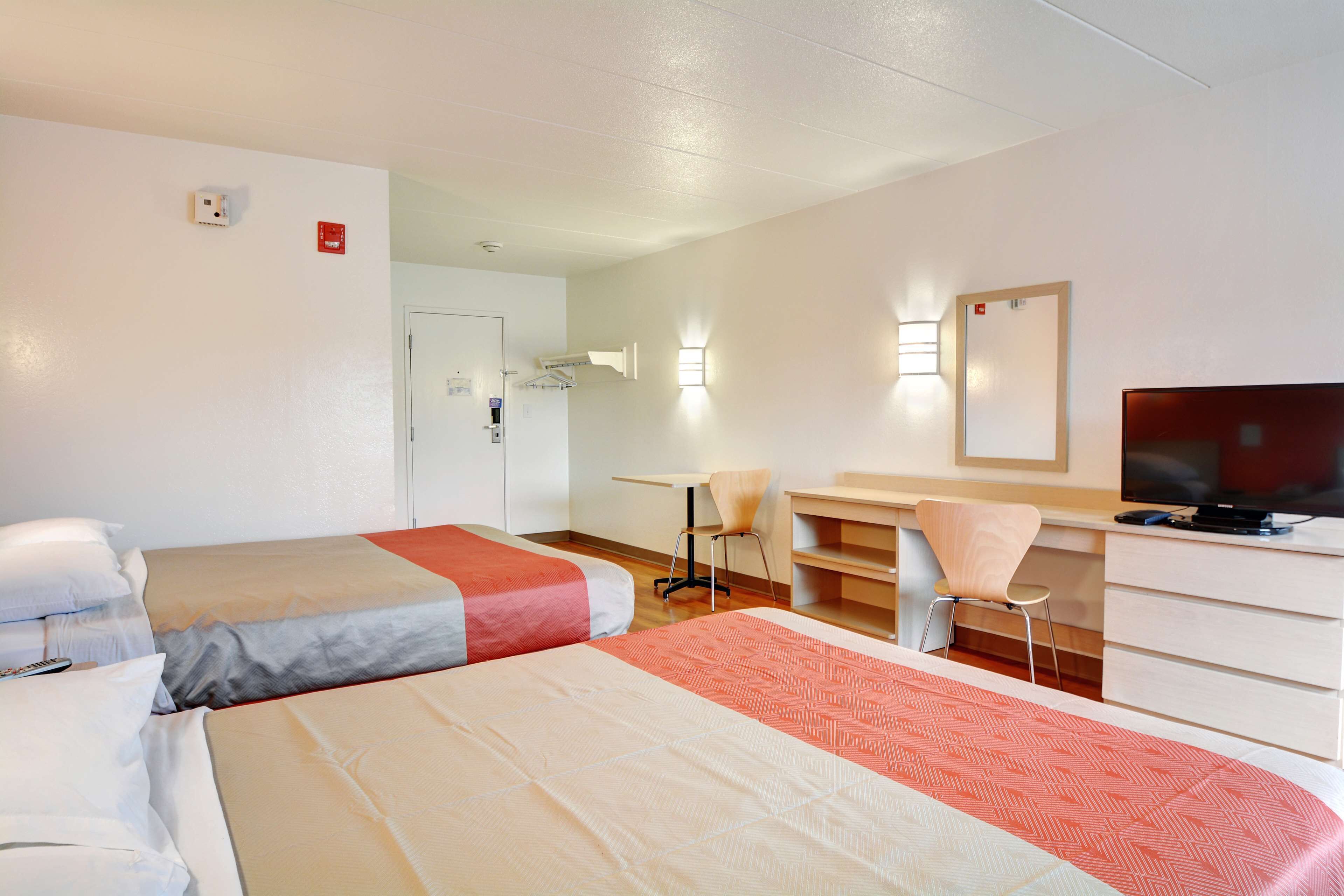Habitación de hotel con dos camas, un escritorio, una silla, un televisor y un espejo.