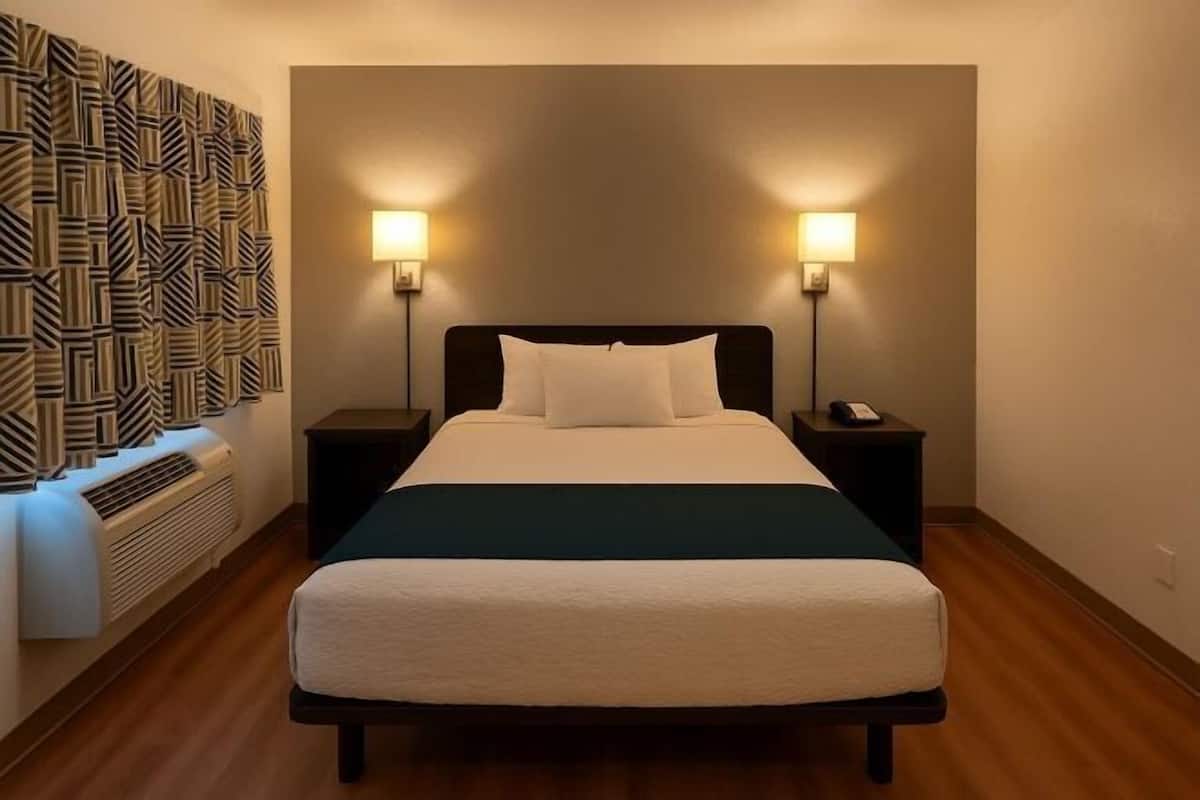 Habitación de hotel con una cama, dos mesitas de noche, un respiradero en la pared y un adorno mural con estampado.