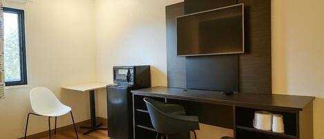 Une chambre moderne et compacte, dotée d’un bureau, de deux chaises, d’un téléviseur à écran plat, d’une petite kitchenette et d’une fenêtre.