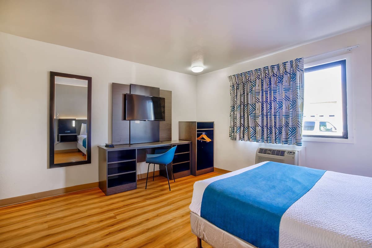 Habitación de hotel con cama, escritorio, silla, armario, televisor y ventana con cortinas.