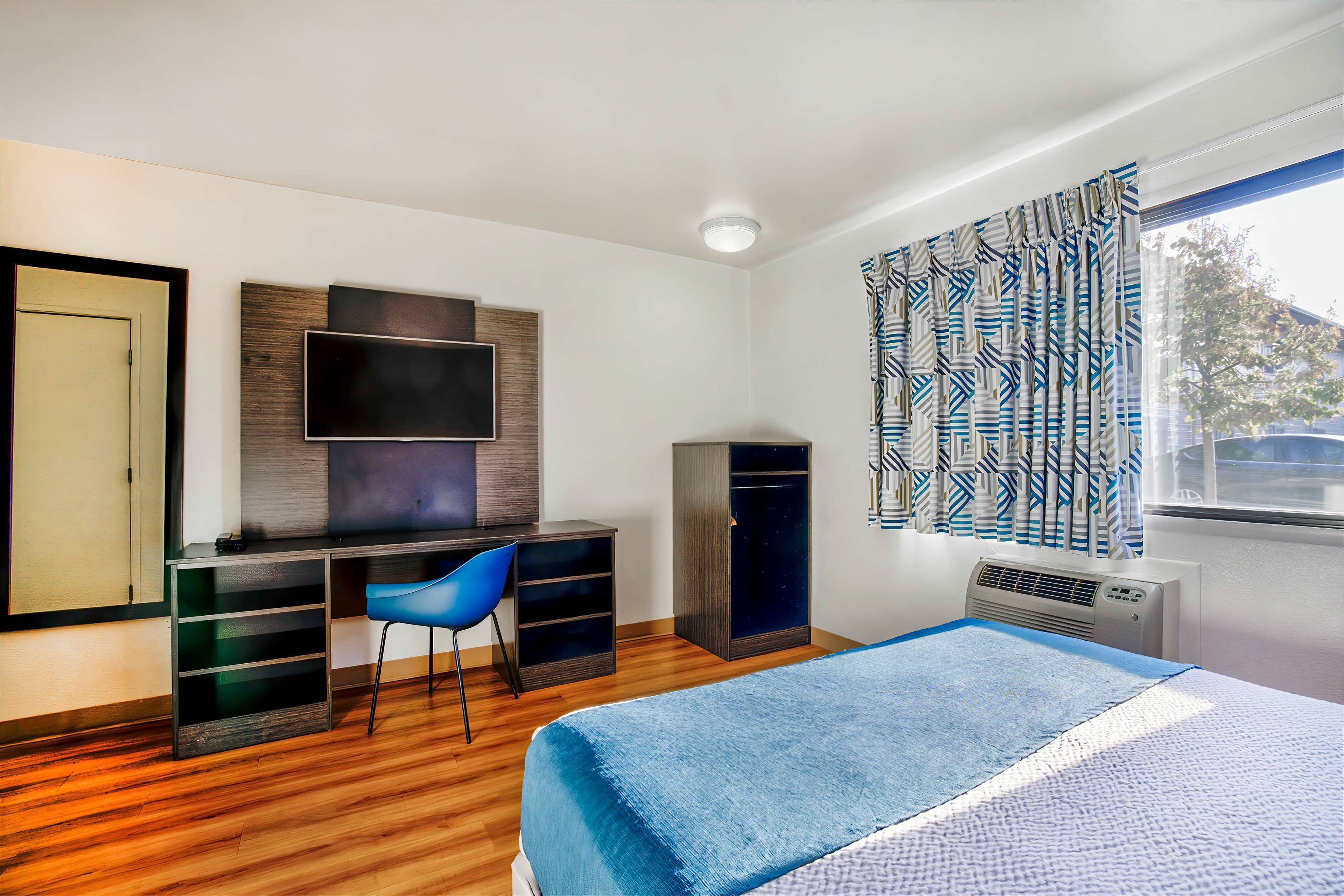 A bedroom with a bed, a desk with a chair, a TV, and a wardrobe.