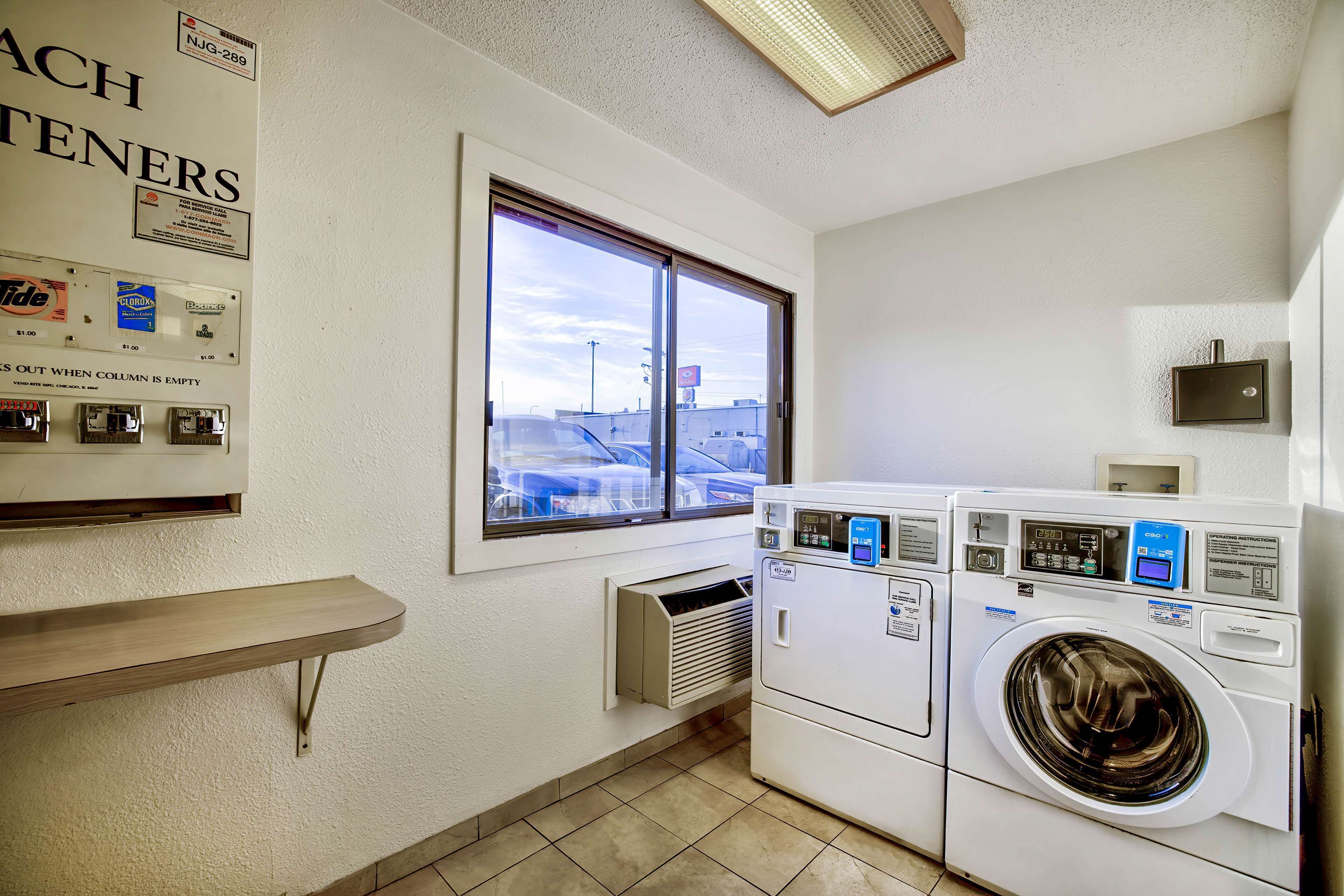 A laundry room with a window, a wall-mounted heater, and a row of dryers.
