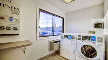 A laundry room with a window, a wall-mounted heater, and a row of dryers.