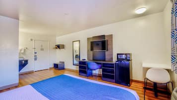 Una habitación de hotel moderna con una cama grande, un escritorio con silla, televisor y microondas.
