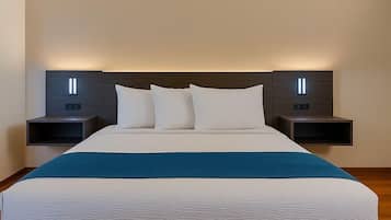 A neatly made bed with a blue accent, flanked by two bedside tables with illuminated panels, in a modern hotel room.