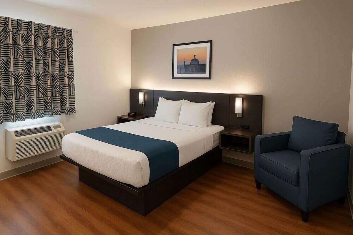 Habitación de hotel con una cama grande, mesitas de noche, una silla, aire acondicionado instalado en la pared y un cuadro enmarcado.