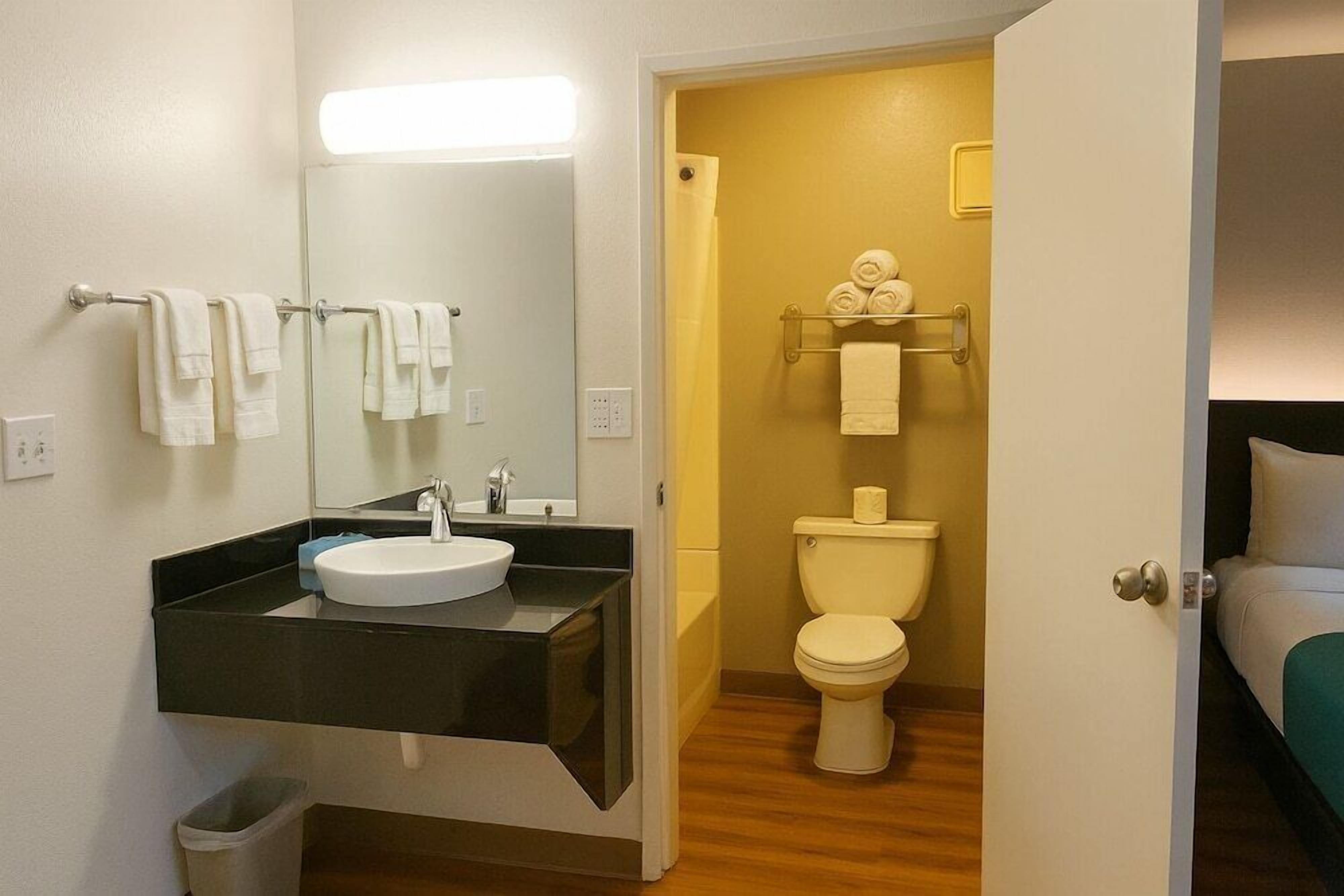 A bathroom with a white sink, mirror, and toilet. There are towels hanging on a rack and a trash bin.