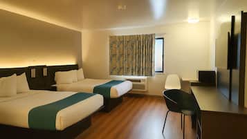 A hotel room with two beds, a desk, a chair, a TV, and a window with patterned curtains.